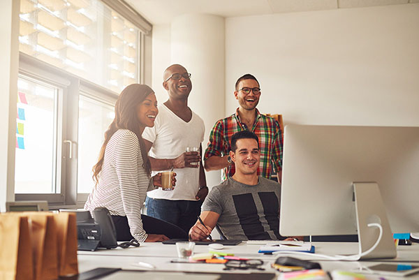 Laughing woman and men at computer in office Office staff uploading Office Makeover video